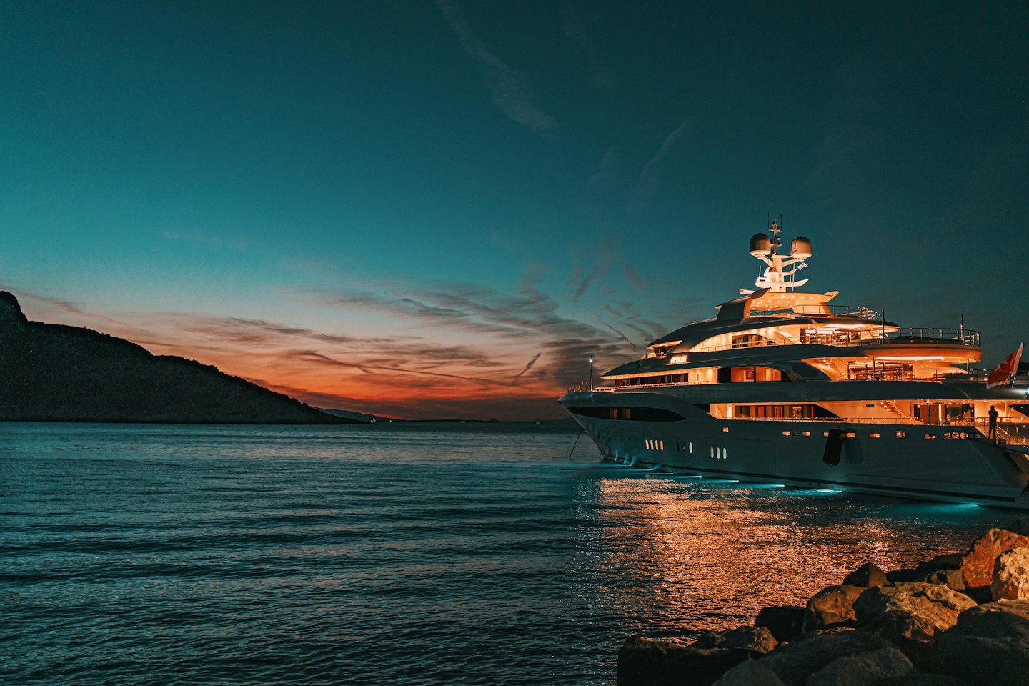 Uno yacht di lusso attraccato su una costa rocciosa al tramonto.