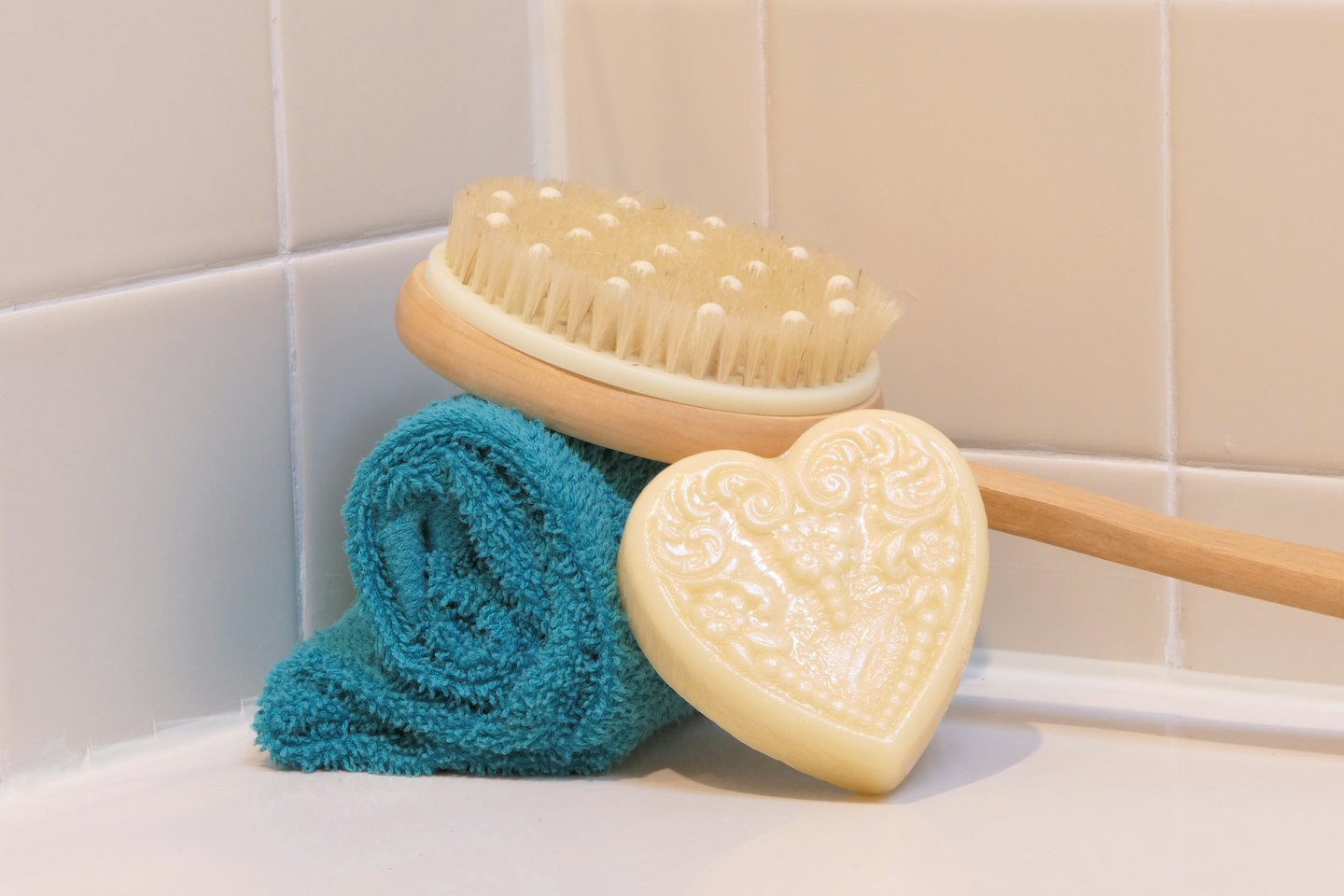 Spazzola per il corpo in legno, asciugamano verde acqua e sapone su superficie bianca.
