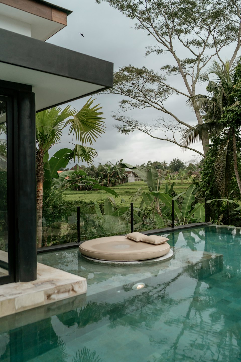 Divano beige accanto a una piscina a sfioro con vista su lussureggianti risaie tropicali.
